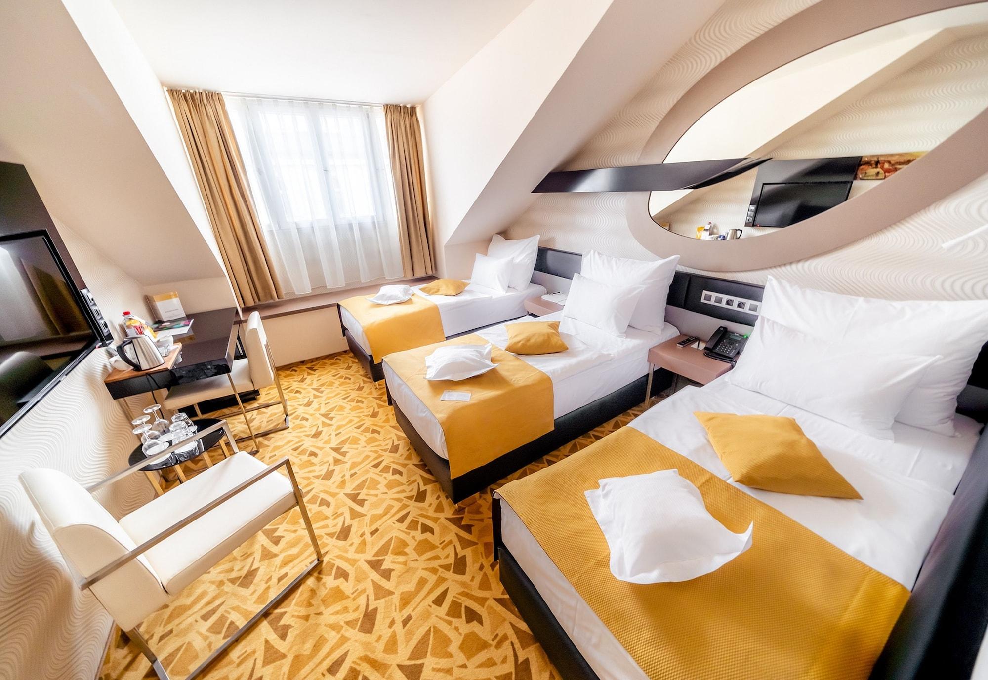 Grandium Hotel Prag Dış mekan fotoğraf The photo shows a hotel room featuring two twin beds, each made up with white linens and yellow decorative pillows. The room has a modern design with a light color scheme, including soft yellow tones. There's a large window letting in natural light, 