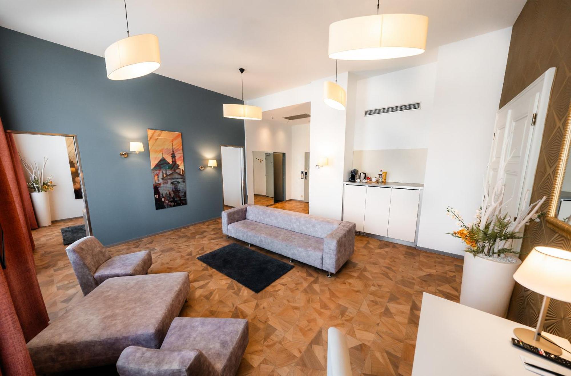 Grandium Hotel Prag Dış mekan fotoğraf The photo shows a modern and stylish living space. The room features light-colored walls and a distinct blue accent wall. There is a large, gray sectional sofa and a small black rug on the wooden floor. The space is well-lit with two pendant lamps ha